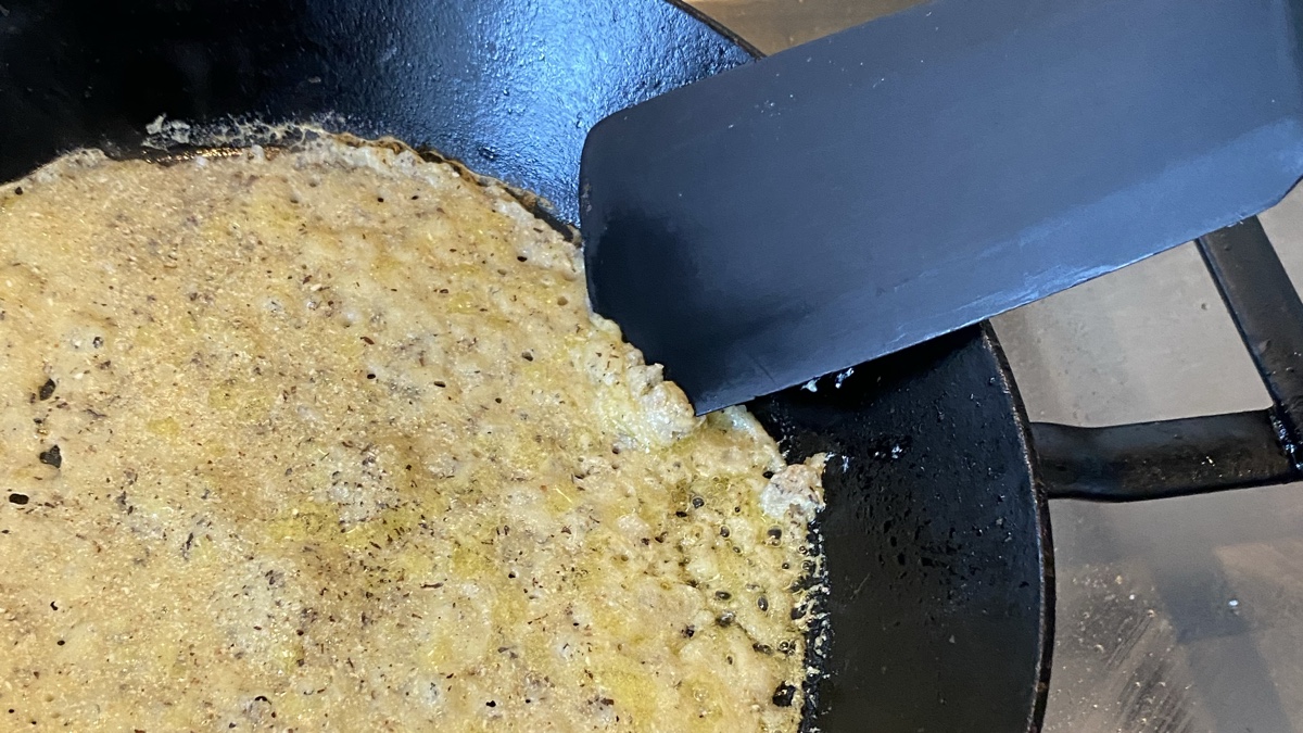 A pale pancake in a black cast iron frying pan with a spatula pushing at the edge of the pancake, which is very weak
