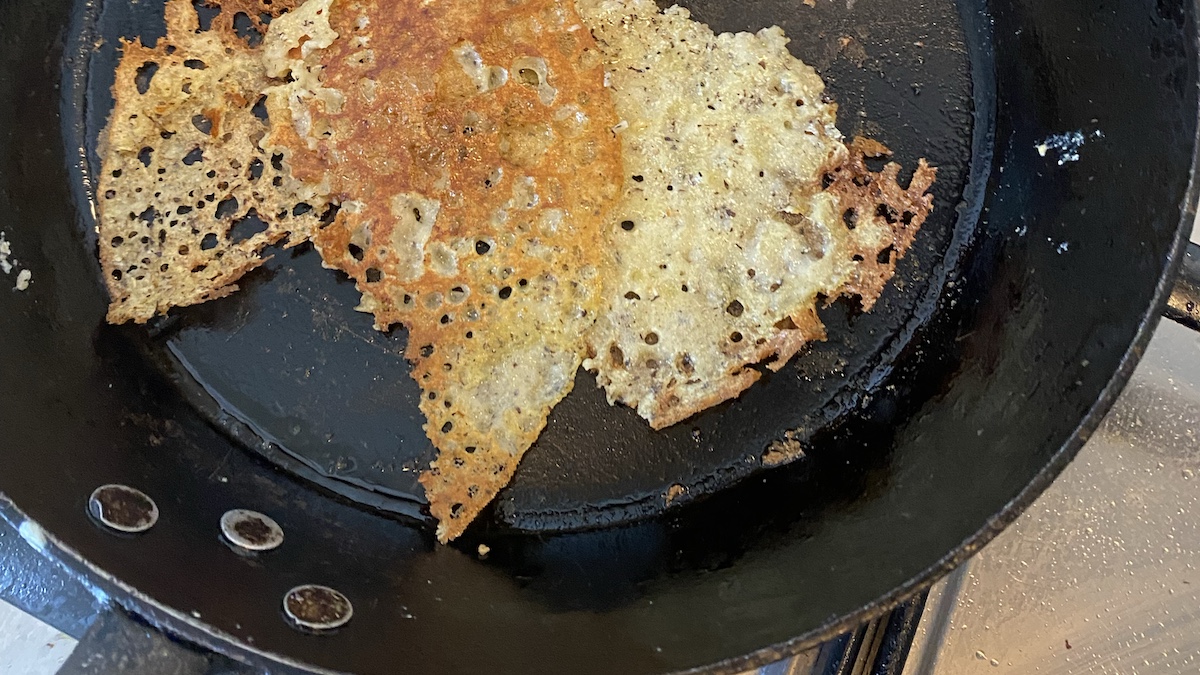 A black cast-iron frying pan containing the broken remnants of a failed buckwheat pancake.