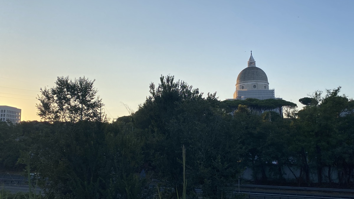 The dome of the church of St Peter and St Paul above a line of green trees with an empty road below them