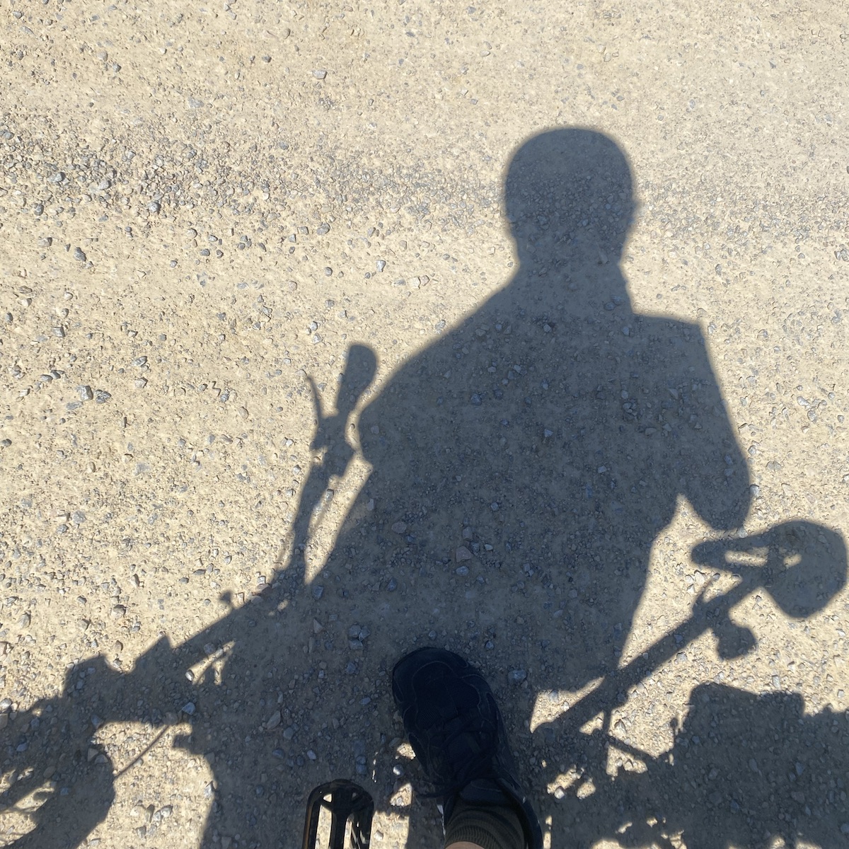 Shadow on the ground on a man on a Brompton bicycle looking at his phone to plan a bicycle tour with Komoot