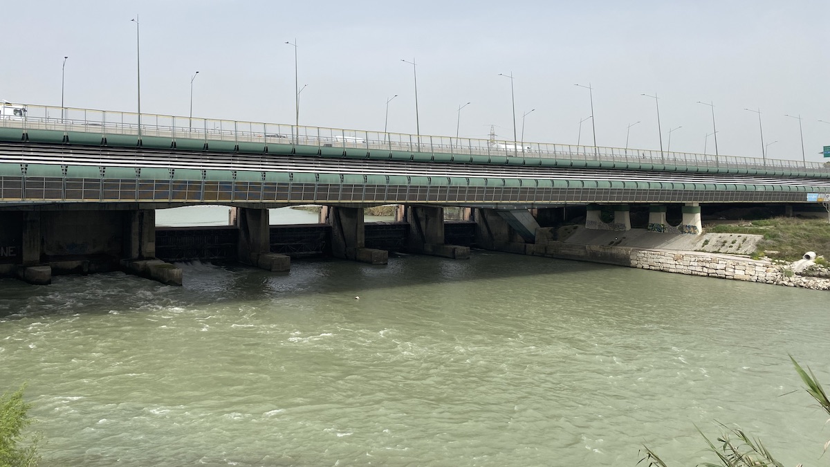 A large concrete bridge over the Tiber river with weirs beneath it to control the flow