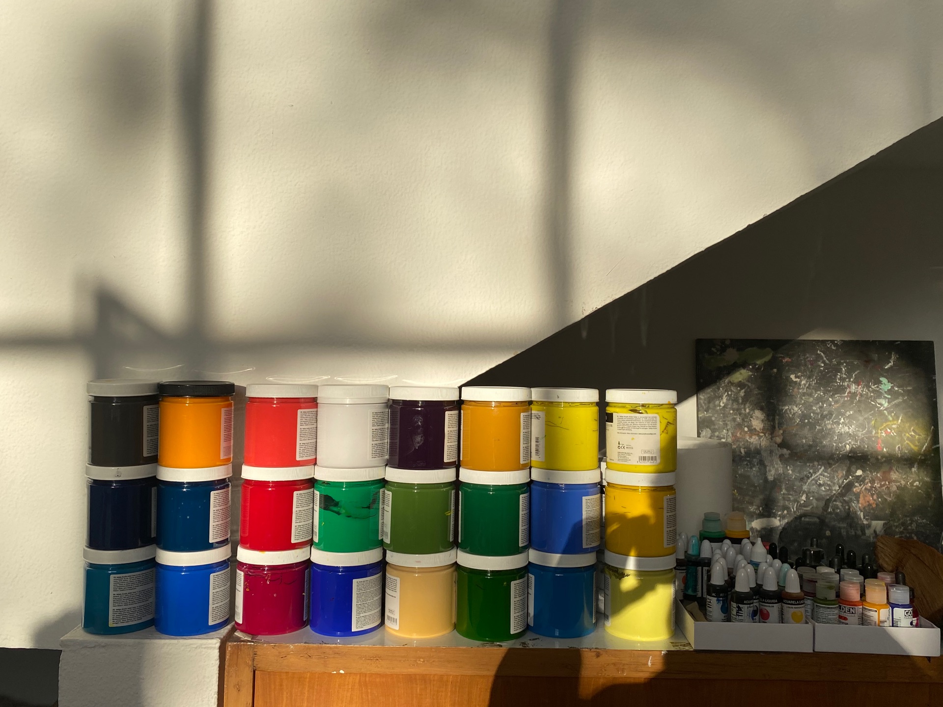 Pots of pigment against a wall, with shadows cast by the window and the photographer